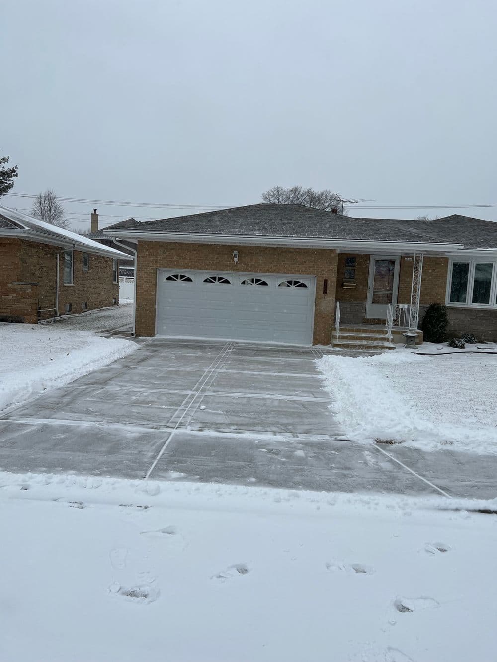 Snow-covered suburban home with a clear driveway and garage in winter weather.
